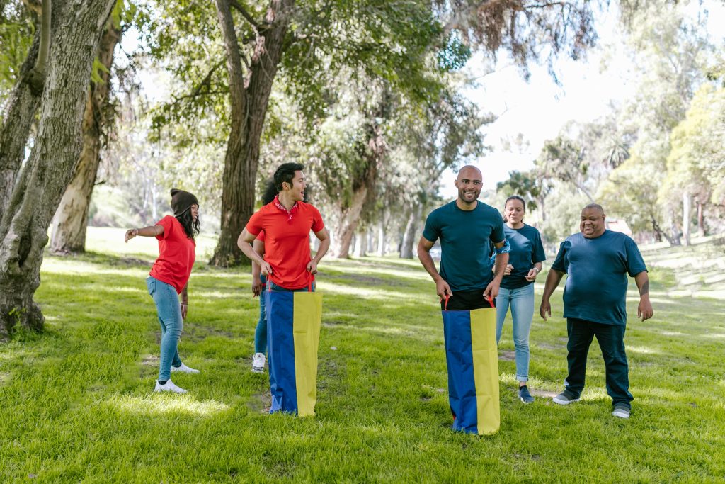 Adults enjoy a lively sack race during a team-building event in a sunny park.